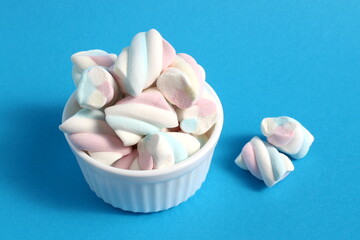 A white cup stands on a blue background with marshmallows.	
