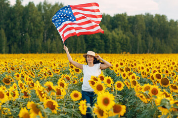 Young woman with American flag in the sunflower field. 4th of July Independence Day USA concept