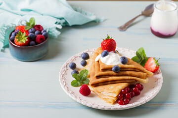 Crepes, thin pancake stack with yogurt and berries. Wrapped pancakes on a plate