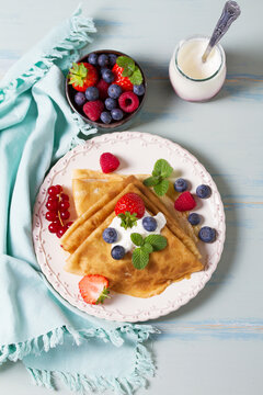 Crepes, thin pancake stack with yogurt and berries. Wrapped pancakes on a plate with copy space. High angle view