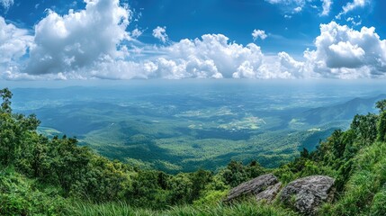 Panoramic landscape view from mountain summit showcasing lush greenery and dramatic cloud formations under a bright blue sky