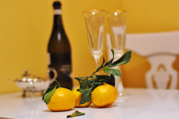 two wine glasses, champagne, tangerines with leaves on a yellow background