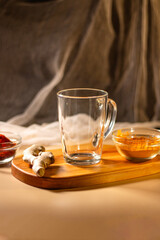 Empty transparent cup on wooden tray with turmeric and chili species. Mock up for design. Served table. Preparation for making drink