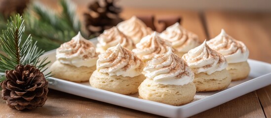 Fototapeta premium Cinnamon star biscuits with frosting arranged on a white plate surrounded by pine branches and cones on a rustic wooden table