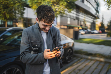 young man drink coffee and use mobile phone in the parking lot