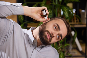 Fototapeta premium Young man suffering from ear pain and puts ear drops in them while sitting at work. Diseases and treatment. Concept of illness, healthy insurance, pharmaceutical, medicine. Ad.