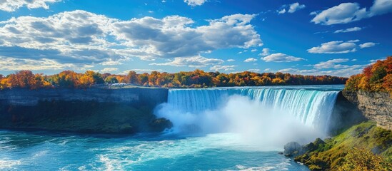 Majestic Niagara Falls cascading into turquoise waters under a vibrant blue sky with fluffy clouds and autumn foliage surrounding the landscape