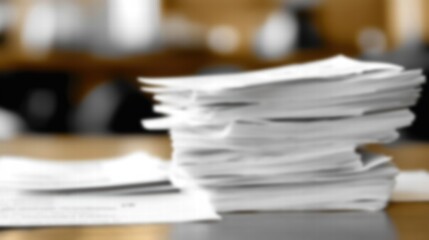 A blurred stack of paperwork on a wooden table, symbolizing busy office life and document management challenges.