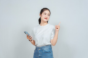 Excited Asian woman pointing at the copy space on top of her while holding her phone, isolated by...