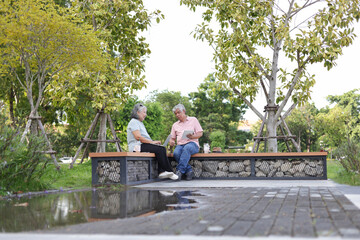 Fototapeta premium Senior couple sitting on a bench in park, Asian senior man and woman use laptop and digital tablet in park