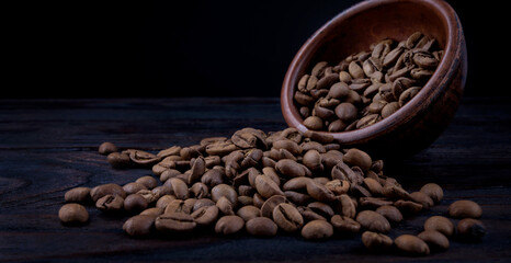 Fototapeta premium Roasted coffee beans spill out of a clay cup onto a wooden surface.
