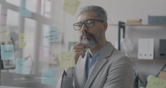 Pensive mature businessman thinking looking at sticky notes focused on problem solving in office. Creative business idea and people concept.