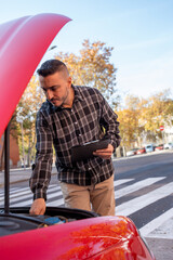 Insurance agent taking notes on clipboard while examining damaged vehicle after road accident