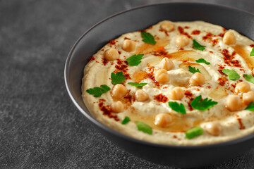 hummus with oil and chickpeas in a dark bowl, selective focus