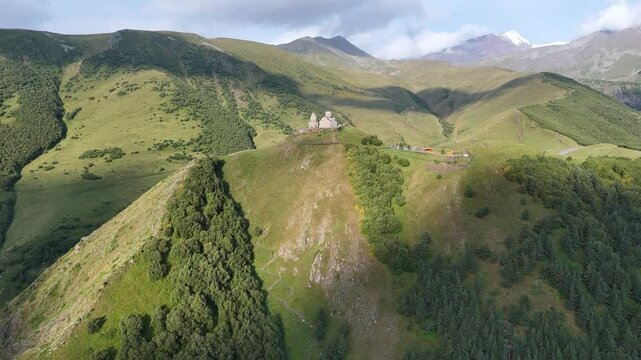 Aerial view of Gergeti Trinity Church in Caucasus Mountains with majestic snow-covered peaks around, near Stepantsminda village in Georgia.