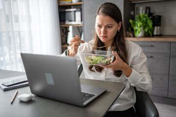 Tired woman eats food ordered at delivery service while sitting in her home office in front of laptop during lunch break. 