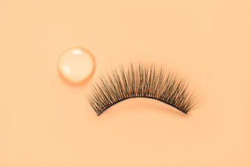 False eyelash and drop of glue on orange background. Women beauty and eyelash extensions.