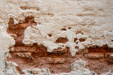 Brick wall with pieces of plaster. Wall of an old building in need of renovation. Aged wall texture of brick building close up. Grunge background with red and white blocks and layers of cement stucco