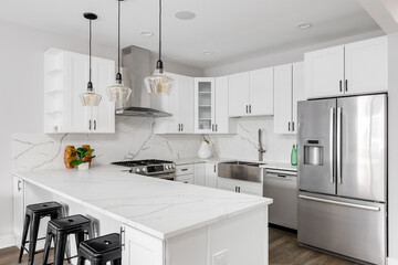 A white kitchen detail with white marble countertop and backsplash, stainless steel appliances,...