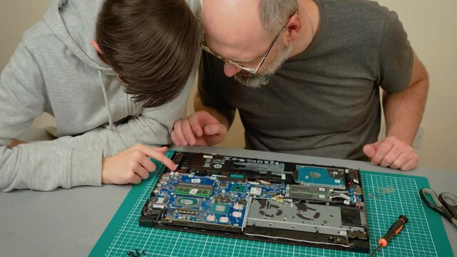 Father explaining components for son, pointing at motherboard and discussing hardware. Male teaching boy about laptop parts, identifying key elements of system. Guy showing kid how internal components