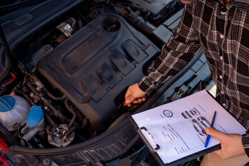 Car mechanic checking the engine oil level and comparing it with the data on the clipboard