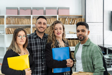 Four business colleagues holding folders and smiling in a modern office with archive files in the background