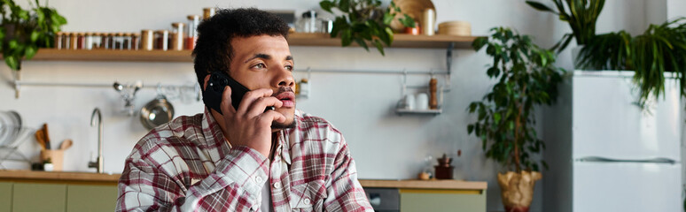 Handsome young man engages in a phone conversation while sitting in a bright kitchen.