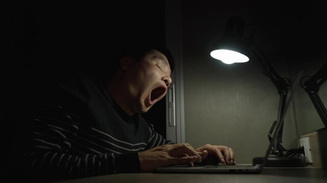sleepy man yawning while working with laptop at night