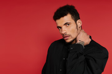Obraz premium A handsome young man stands with a stylish demeanor in front of a bright red background.