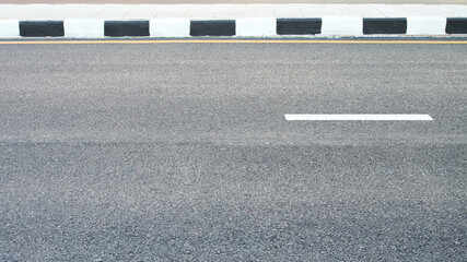 Clean asphalt road with a white lane marking and black-and-white painted curb, highlighting urban infrastructure and transportation design.