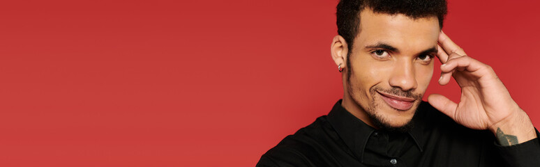 Obraz premium A young man poses confidently with a smile while touching his face, showcasing charm and style.