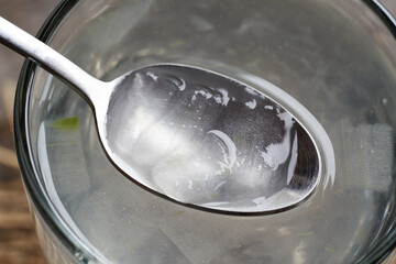 Fresh aloe vera pulp or flesh on a spoon above a glass of aloe vera juice