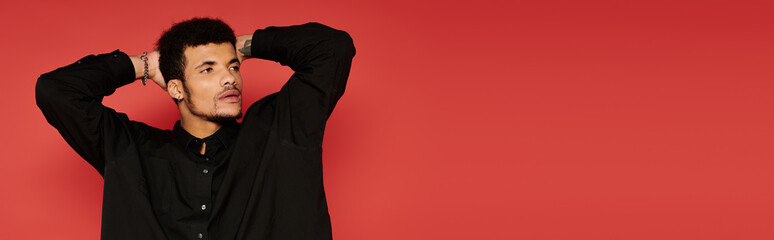 A young handsome man with stylish hair poses confidently in a black shirt against a red backdrop.
