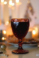 Various Christmas decorations, cookies, chocolate, nuts and tangerines, wine glasses and lit candles on the table. Holiday hygge at home. Selective focus.