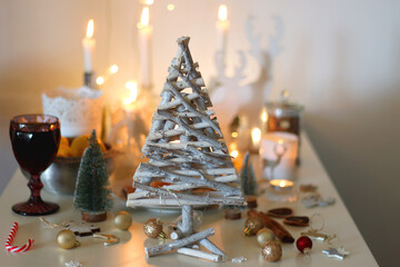 Various Christmas decorations, cookies, chocolate, nuts and tangerines, wine glasses and lit candles on the table. Holiday hygge at home. Selective focus.
