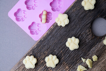 Paw print shaped moisturizing balm for dog or cat paw pads on a rustic cutting board with a bright pink mold.