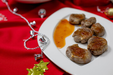 Close-up of seared meat medallions served with a vibrant sauce on a white plate, decorated with Christmas ornaments on a festive red tablecloth.
