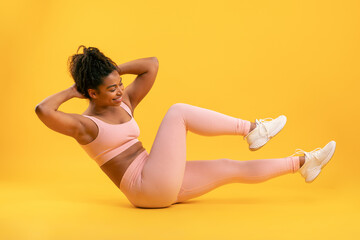 A woman performs an ab workout by holding her legs up while leaning back against a vibrant yellow...