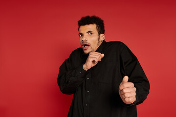 Young handsome man appears startled while posing against a bright red background.