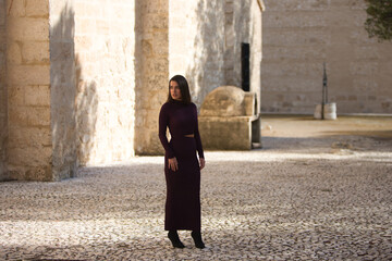 pretty young woman dressed in elegant violet dress posing on a cobblestone street next to a monastery in a village in the city of Seville, Spain. The woman makes different expressions and gestures.