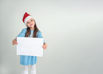 Cute smiling girl in Santa Claus hat with a white blank paper sheet, copy space. Christmas and New Year sale concept. Mockup for advertising.