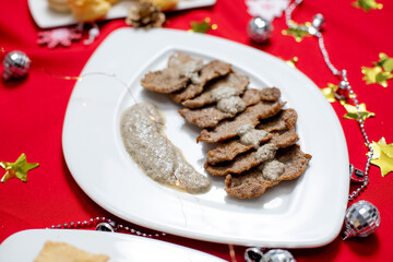Festive holiday table with a variety of dishes including salads, meat, and appetizers, decorated with Christmas ornaments and pinecones on a red tablecloth.
