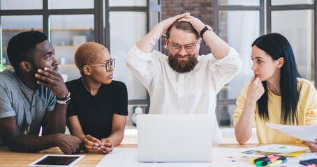 Group of confused multiethnic coworkers using laptop at office