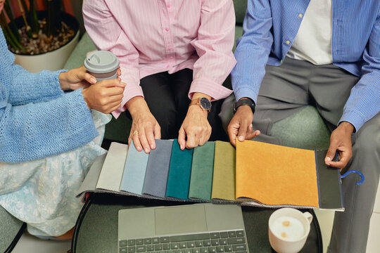 Cropped shot of diverse group of three interior designers choosing fabric on samples in different colors while working collaboratively at table in coworking lounge area