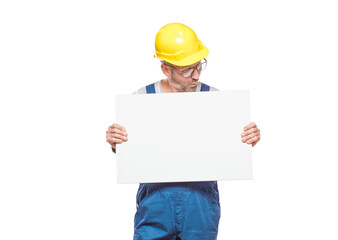 Surprised construction worker holding white board, isolated on white background. Promoting repairman showing blank empty paper billboard with blank space for text. Craftsman against white wall