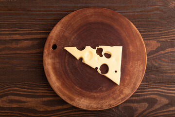 Piece of cheese with holes on cutting board on brown wooden, top view, copy space
