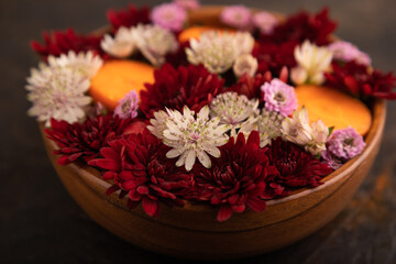 wooden bowl with carrot slices and red Chrysanthemum flowers, Astrantia flowers, flower salad on black concrete, side view, close up, selective focus
