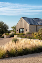 Obraz premium A modern farmhouse in the central valley of Texas, surrounded by native plants and perennials,creating an oasis atop rolling hills.The house features light-colored stone walls with bronze metal accent