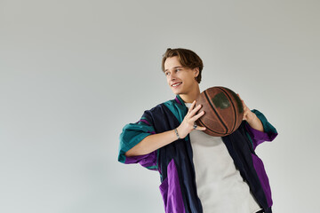 A confident young man in a trendy bomber jacket poses with a basketball in a modern studio space.