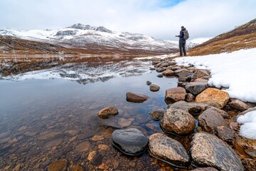 Fototapeta premium A person standing by the edge of a fjord, skipping stones across the smooth, reflective water